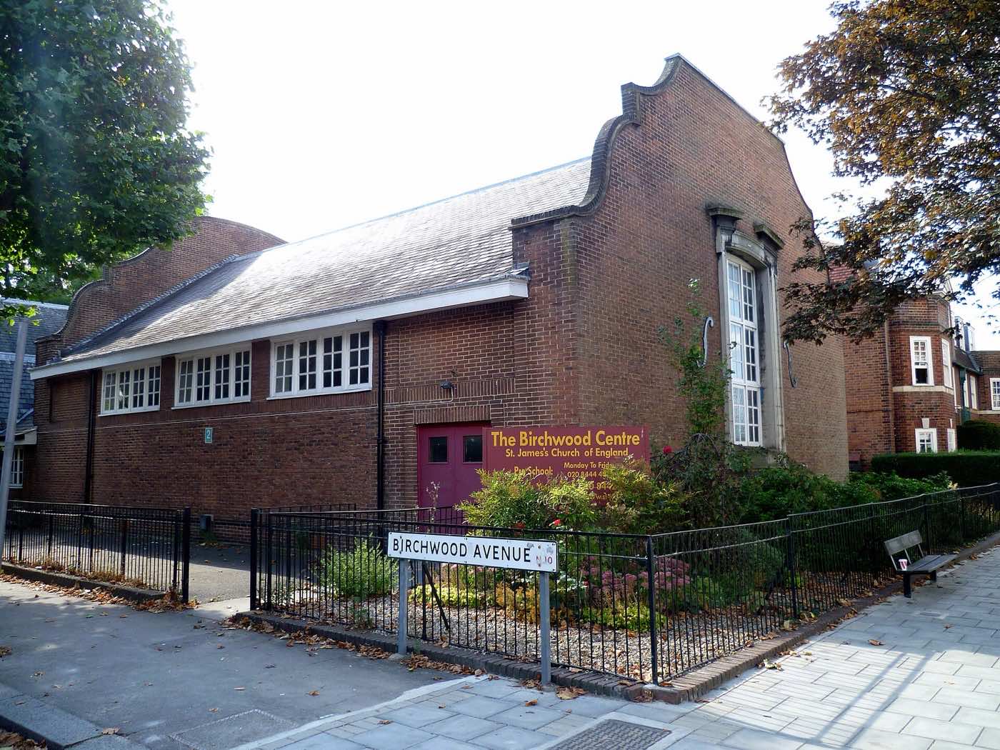 St James Church Hall in Muswell Hill: a red-brick hall with a curved gable and a row of high windows, behind railings on a street corner
